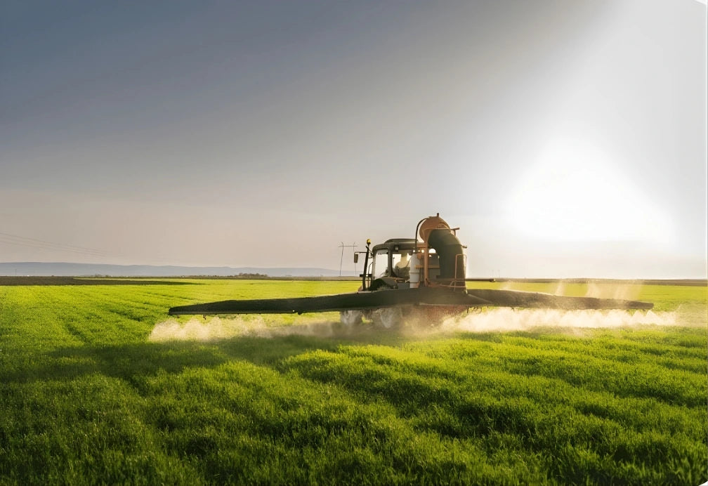 Tractor spraying a field with a bright light source in the background
